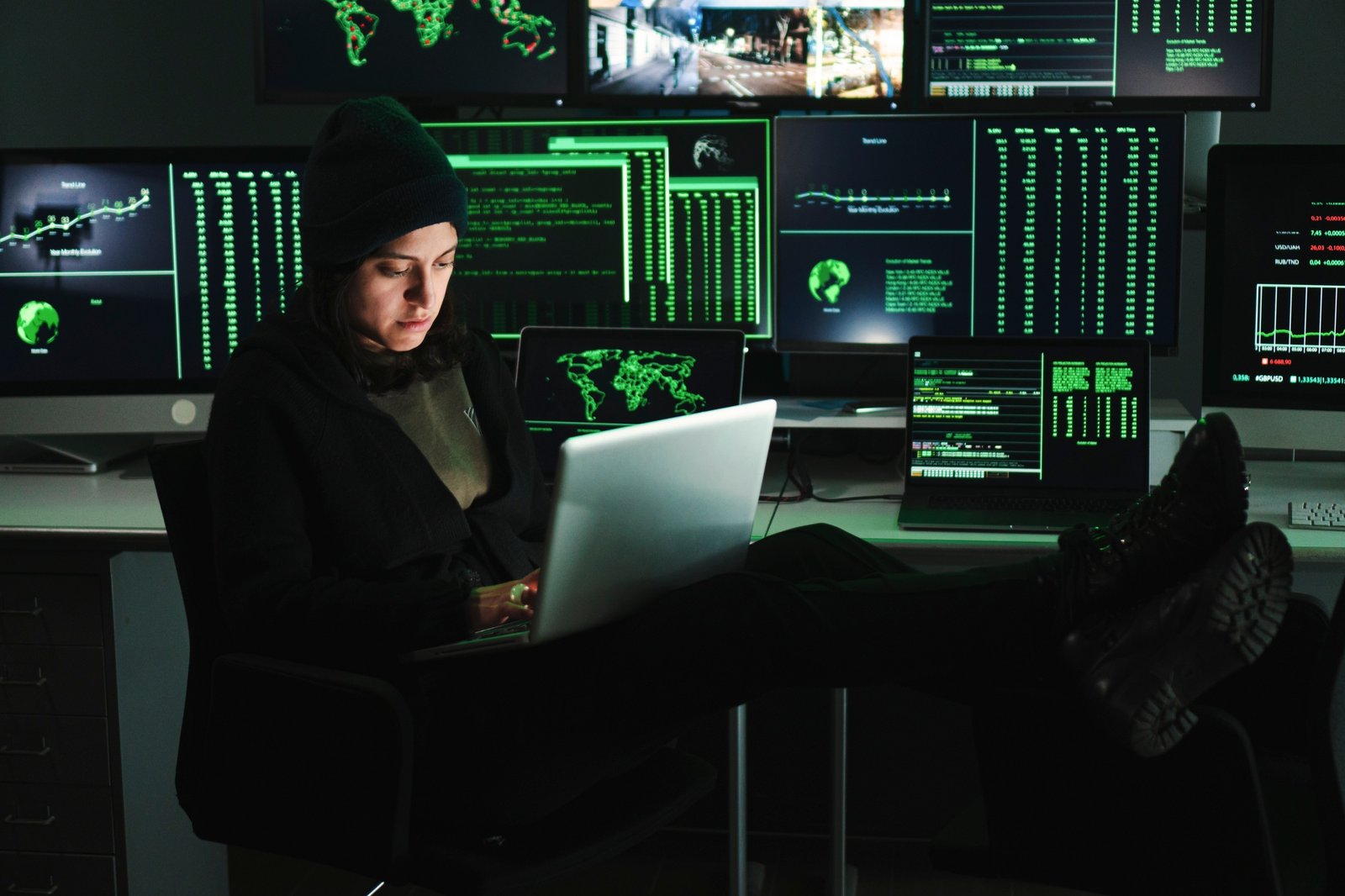 Informatic hacker woman typing code on laptop, at background a lot of computer screens with data